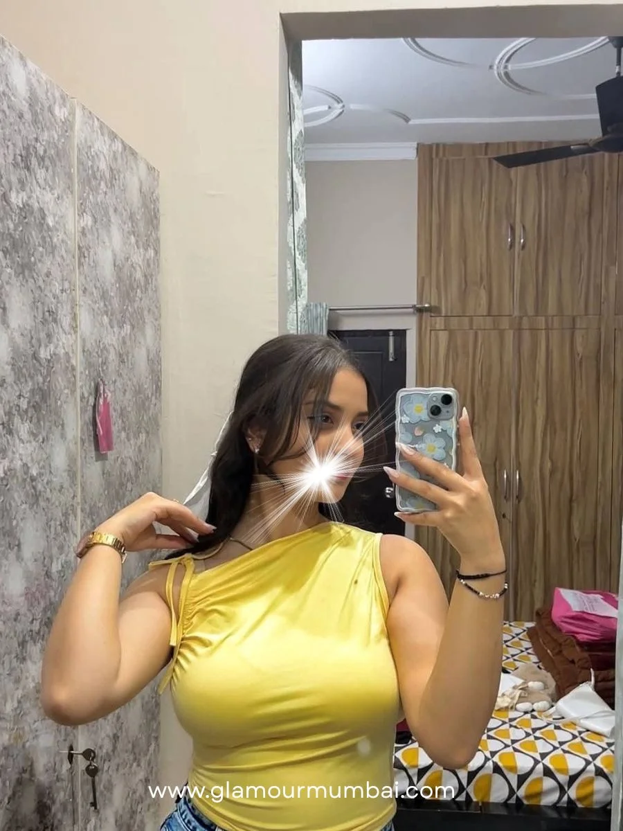 Meet Pallavi escort in Mumbai wearing yellow outfit, standing indoors near mirror and wooden wall panel.