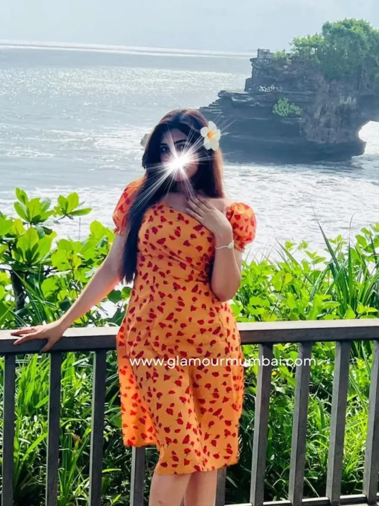 Nancy elite escort wearing an orange floral dress with a scenic sea view background